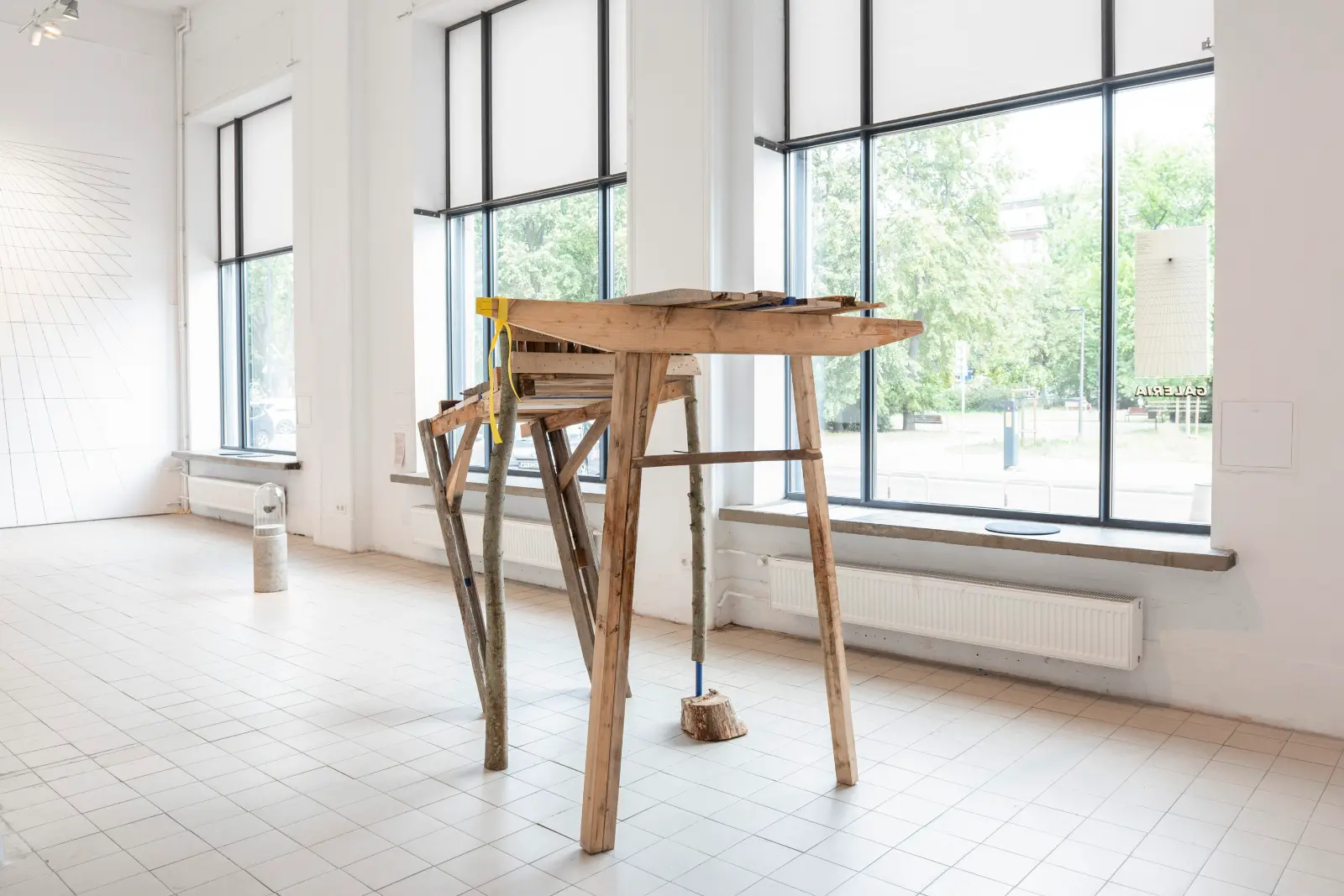 Drewniana instalacja przypominająca częściwo byka lub tura, a częściowo most. Praca stoi w białym pomieszczeniu galeryjnym.