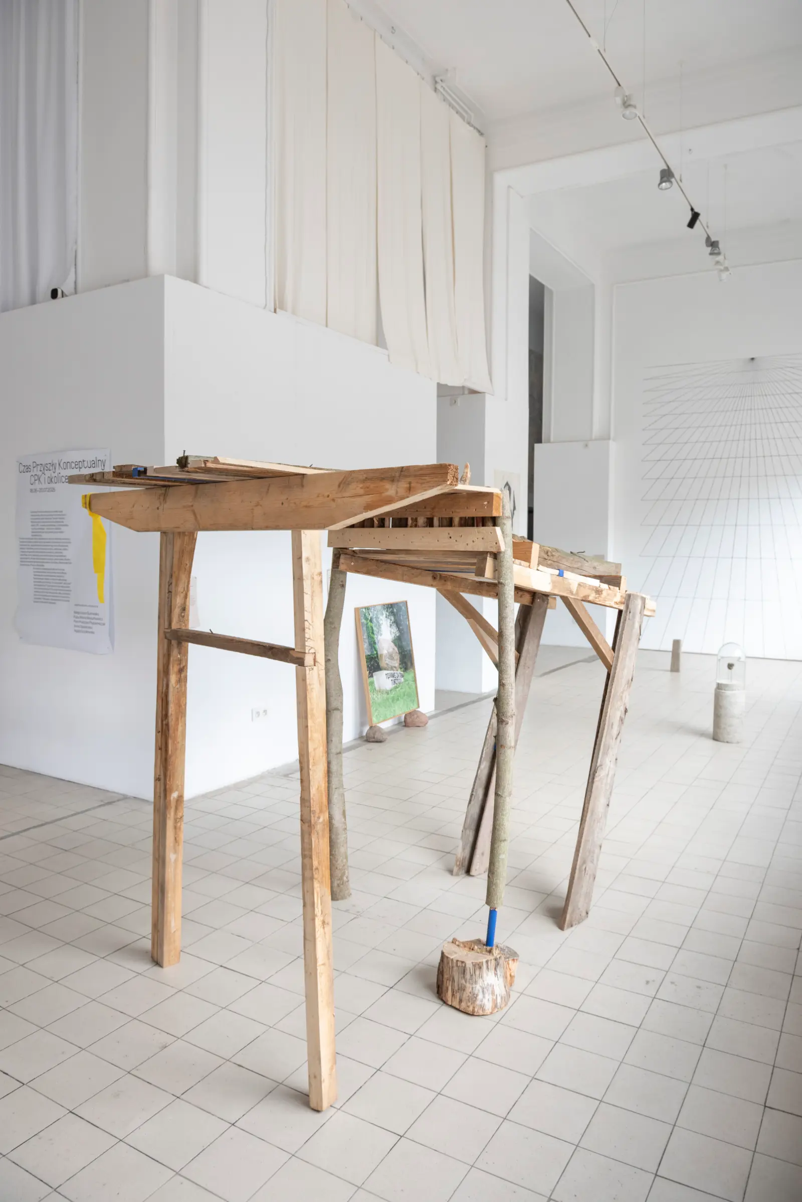 Drewniana instalacja przypominająca częściwo byka lub tura, a częściowo most. Praca stoi w białym pomieszczeniu galeryjnym.