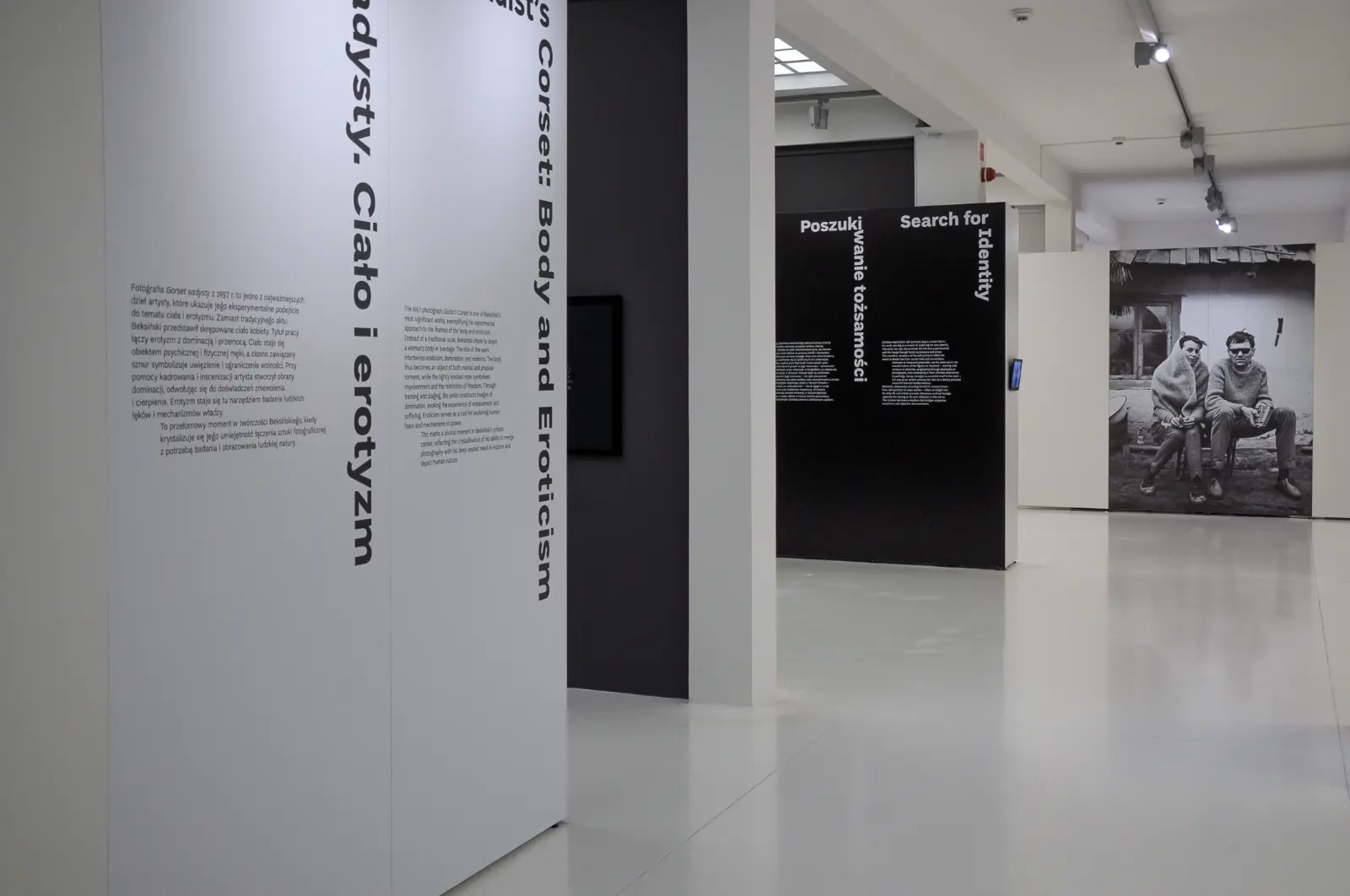 Widok wystawy „Fenomenalny. Zdzisław Beksiński”. Na pierwszym planie teksty kuratorskie, w tle wielkoformatowe zdjęcie przedstawiające autora z żoną.
