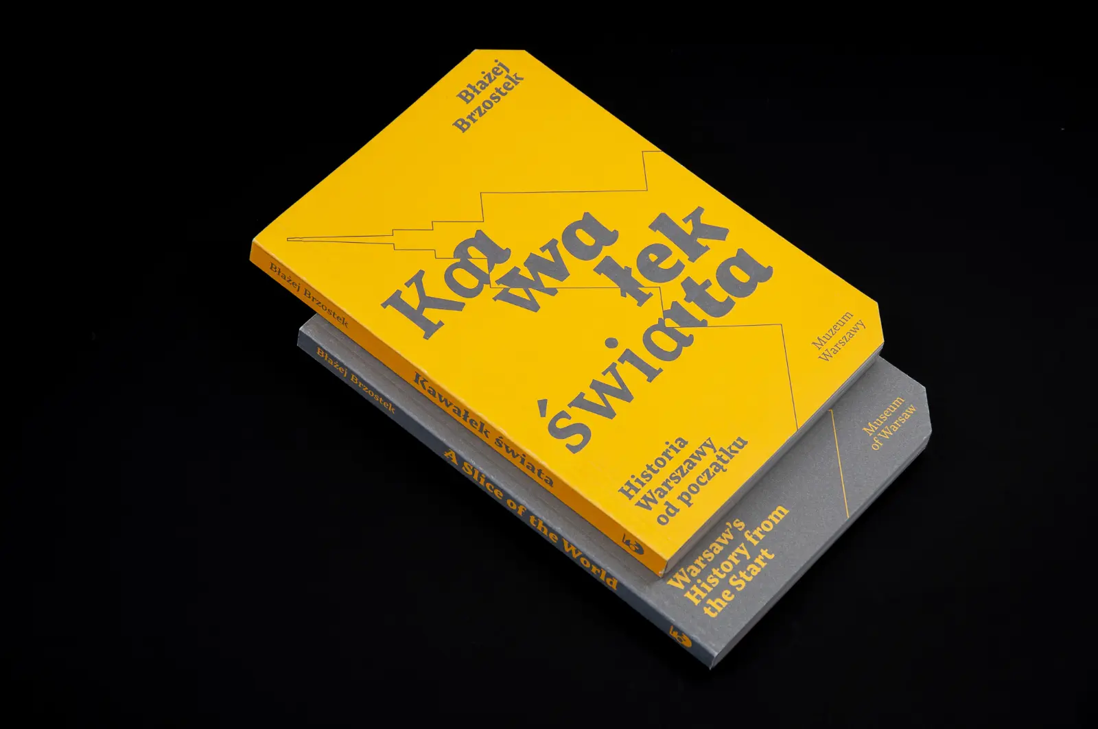 Two books stacked on top of each other. On top is the yellow Polish version of “A Slice of the World,” and underneath is the gray English one.