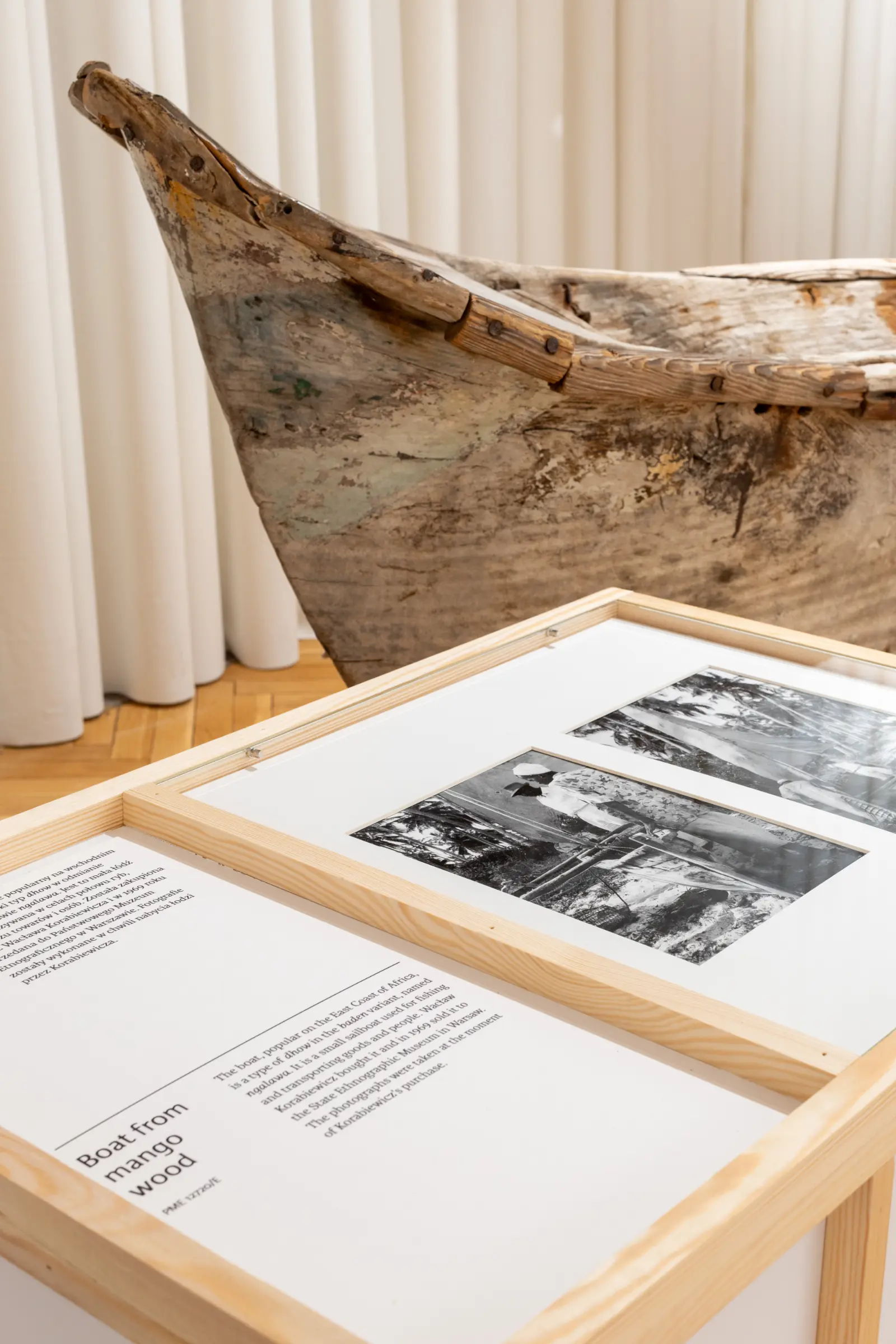 View of the exhibition. Display cases with artifacts in the foreground. Further away, there is a fragment of an old boat.